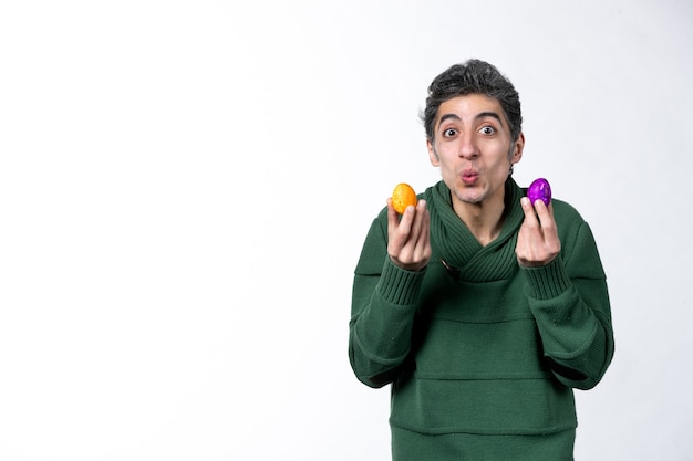 Photo front view of young man holding colored painted eggs on white wall