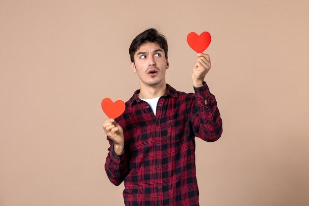 Front view young man holding red heart stickers on brown wall