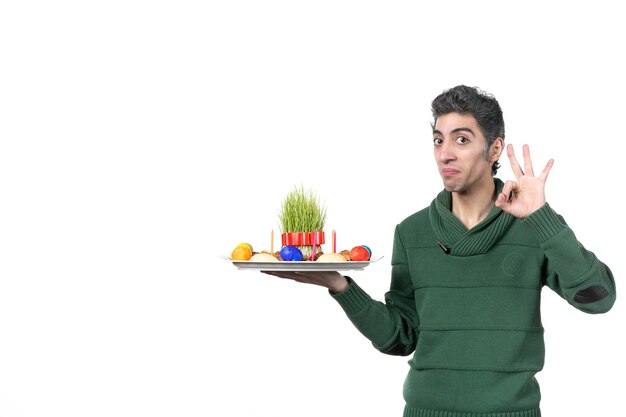 front view of young man holding traditional novruz xoncha on white wall