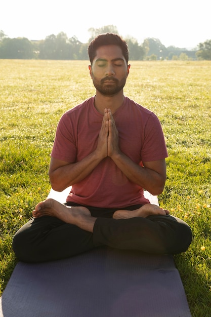 Front view of young man meditating outdoors on yoga mat