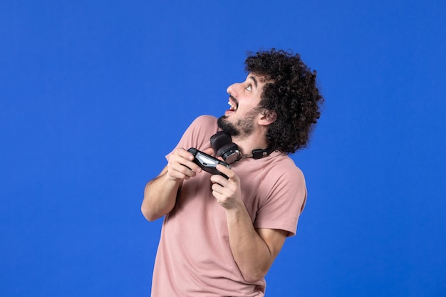 Front view young man playing video game with black gamepad on blue background virtual teen youth sofa adult soccer player winning joy