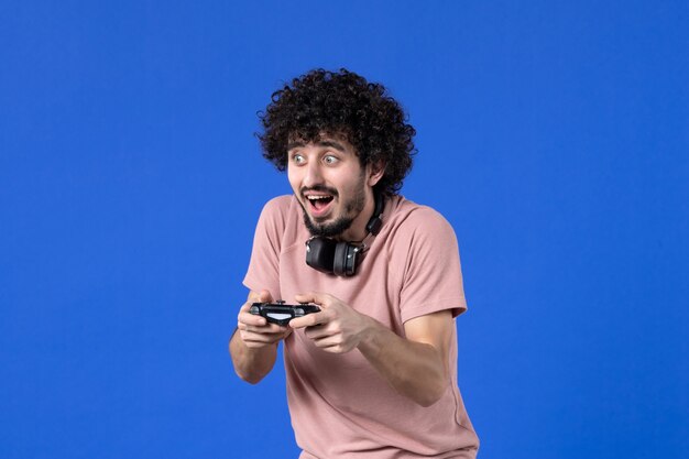 front view young man playing video game with black gamepad on blue background virtual teen youth sofa adult soccer player winning