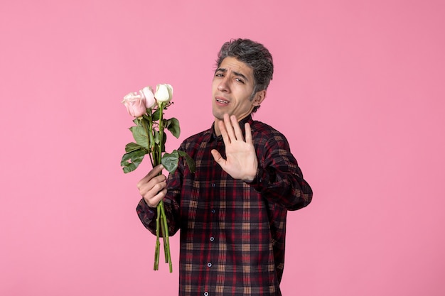 Front view young man posing with beautiful pink roses on pink wall