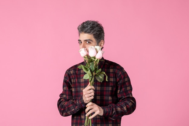 Front view young man with beautiful pink roses on pink wall