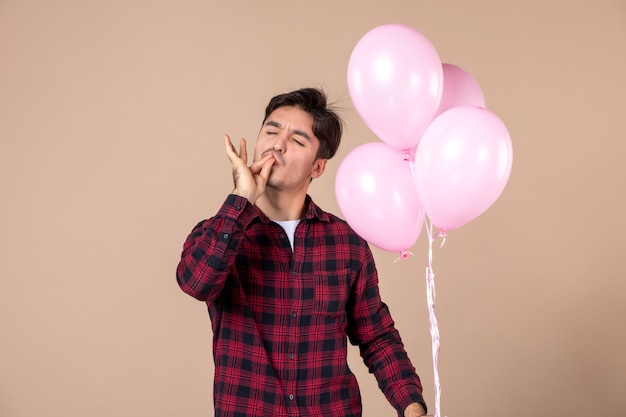 Vista frontale giovane con palloncini rosa sulla parete marrone Foto Premium