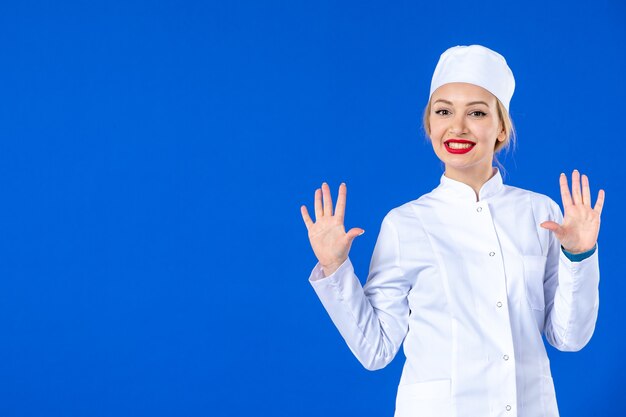 front view of young nurse in medical suit on blue wall