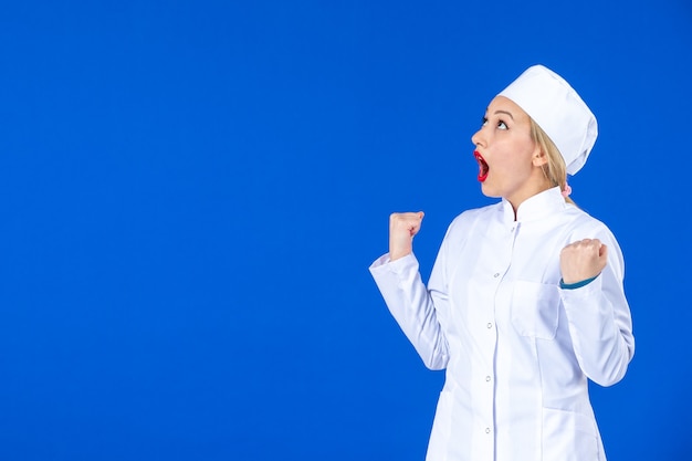 front view of young nurse in medical suit on blue wall