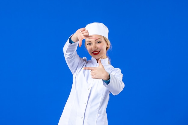 front view of young nurse in medical suit on blue wall