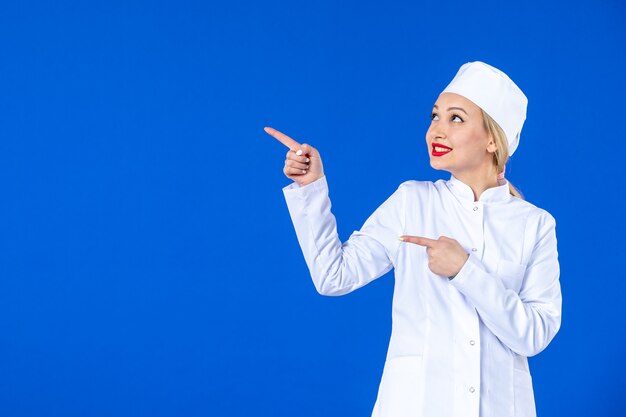 front view of young nurse in medical suit on blue wall