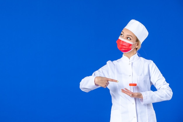 front view young nurse in medical suit with mask holding flask on blue background drug virus covid- hospital doctor vaccine pandemic health medicine photo