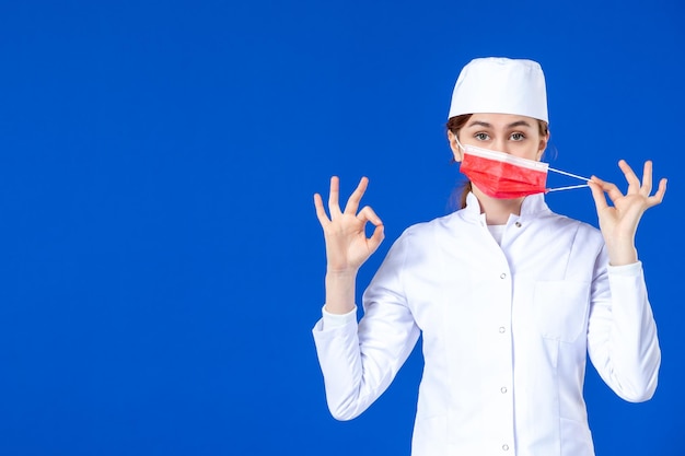 Front view of young nurse in medical suit with red mask on blue