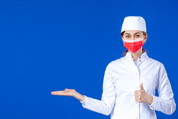 Front view of young nurse in medical suit with red mask on blue 