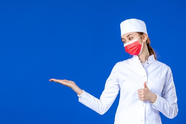 Front view of young nurse in medical suit with red mask on blue 