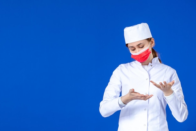 Front view of young nurse in medical suit with red mask on blue 