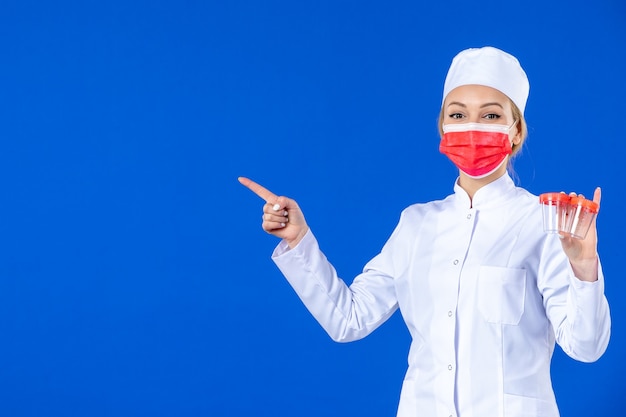 front view young nurse in medical suit with red mask holding flasks on blue background drug health doctor covid- hospital virus medicine