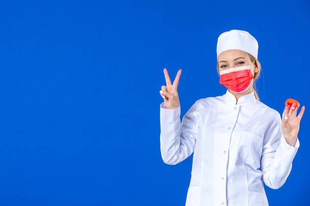 front view young nurse in medical suit with red mask holding flasks on blue background pandemic covid- medicine doctor health drug virus