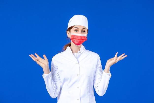 Front view young nurse in medical suit with red protective mask on blue wall