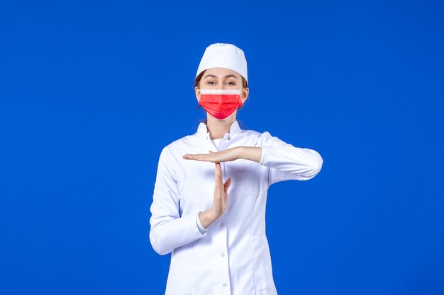 Front view young nurse in medical suit with red protective mask on blue wall