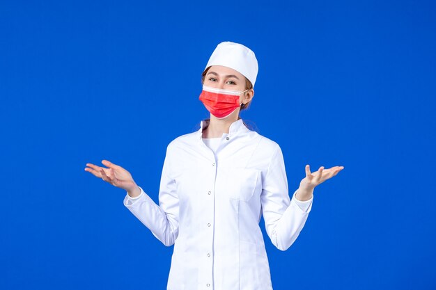 Front view young nurse in medical suit with red protective mask on blue wall