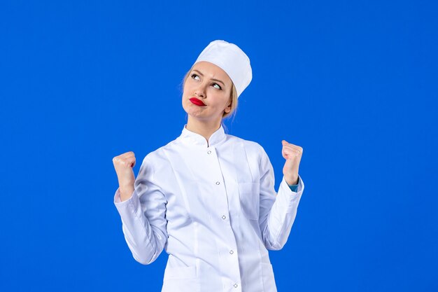 front view of young nurse in white medical suit on blue wall