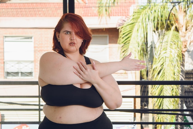 Front view of young plus size woman in black sportswear stretching and looking at the camera