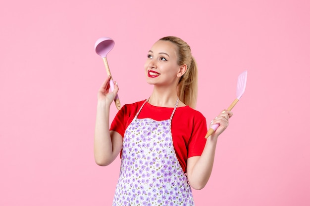Front view young pretty housewife in cape holding spoons on pink wall