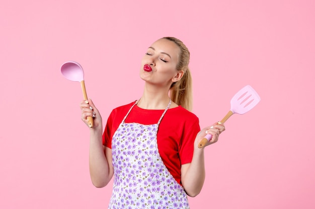 Photo front view young pretty housewife in cape with spoons on pink wall