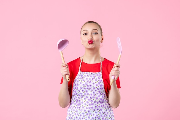 Front view young pretty housewife in cape with spoons on pink wall