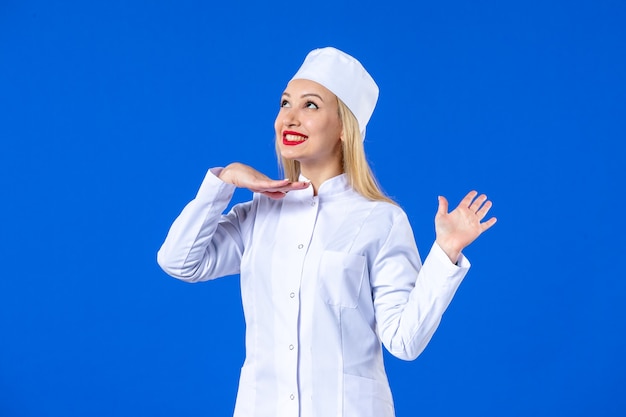 front view of young pretty nurse in medical suit on blue wall