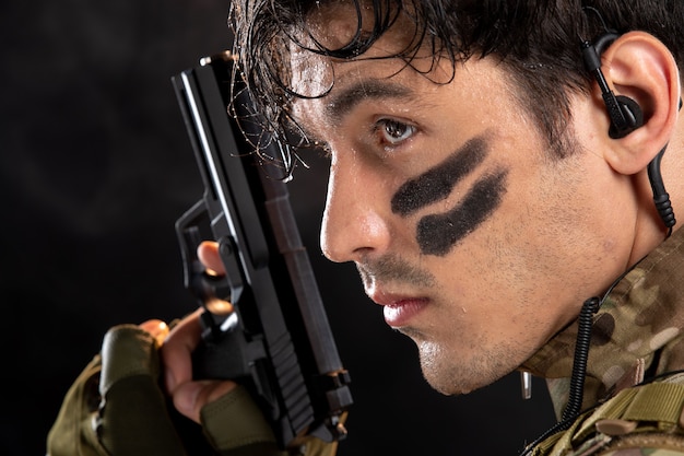 Front view of young soldier in camouflage aiming gun on black wall