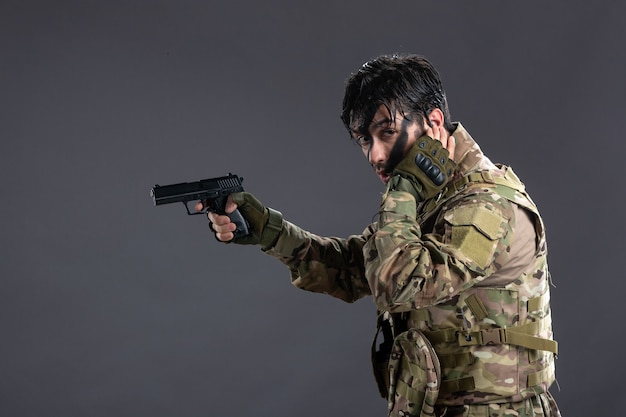 Front view of young soldier in camouflage aiming gun on dark wall