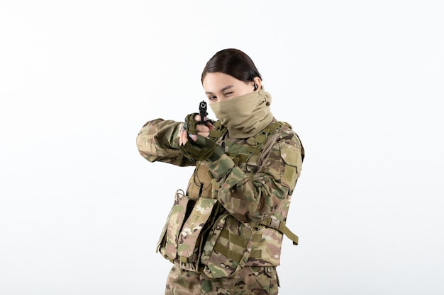 Front view of young soldier in camouflage aiming gun on a white wall