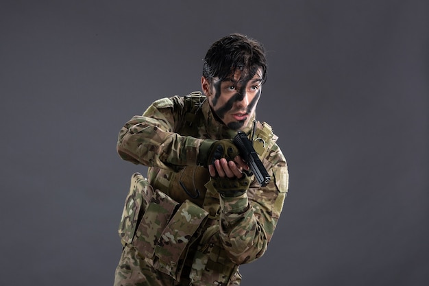 Front view of young soldier in camouflage with gun dark wall