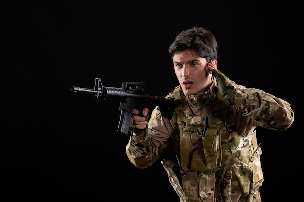 Front of view young soldier in uniform on the black wall