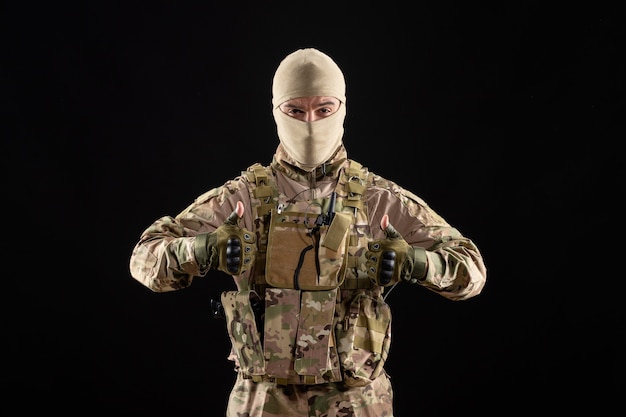 Front view young soldier in uniform on a black wall