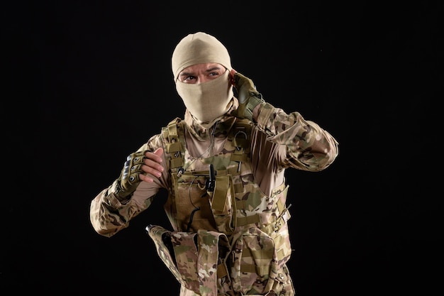 Front view of young soldier in uniform and mask on black wall