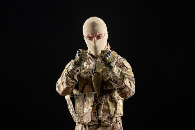 Front view of young soldier in uniform and mask on black wall