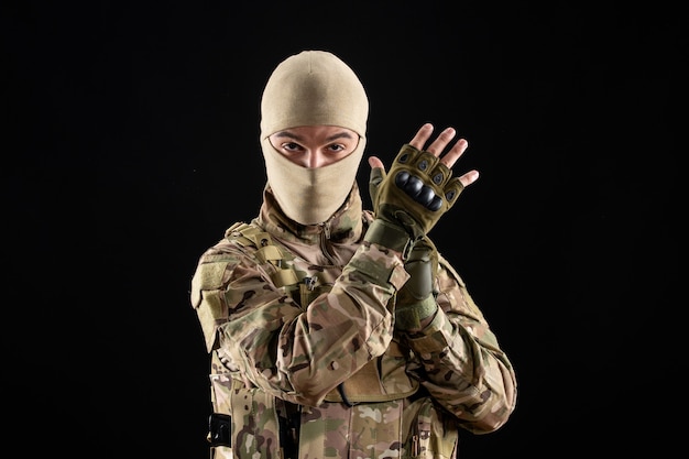 Front view of young soldier in uniform wearing gloves on black wall