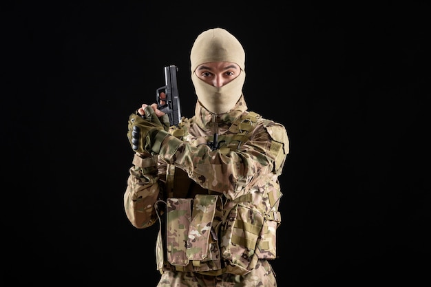 Vista frontale del giovane soldato in uniforme con la pistola sul muro nero