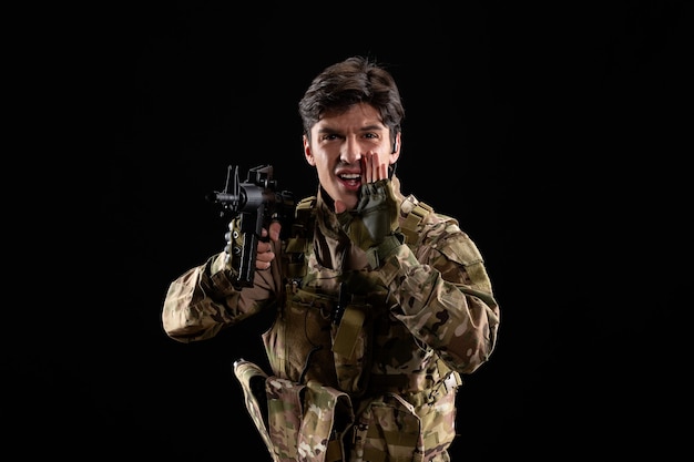 Front view of young soldier in uniform with rifle on black wall