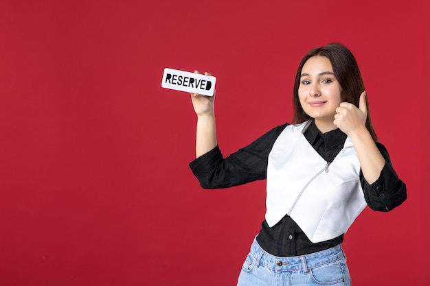 front view young waitress holding reserved written nameplate and smiling on red background uniform color work woman job dinner beauty food restaurant meal