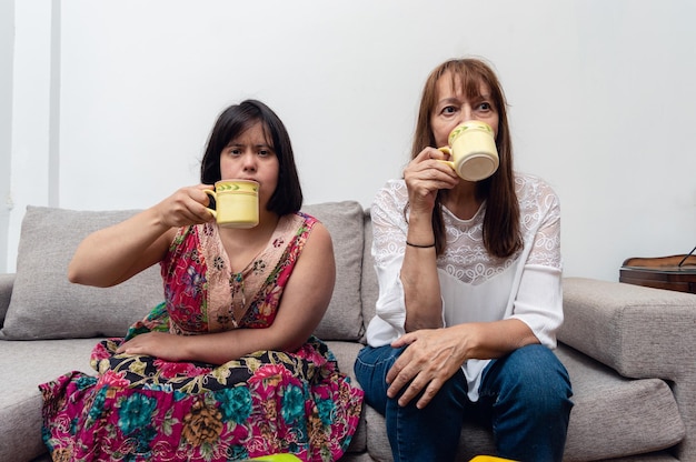 Front view of young woman with down syndrome sitting having a cup of coffee with her mom