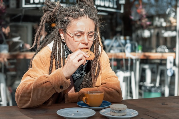 카페테리아 밖에 앉아 choloate 쿠키를 먹고 dreadlocks와 젊은 여자의 전면 모습