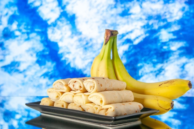 Front view yummy rolled pancakes with bananas on blue background sweet dessert morning color milk breakfast cake sugar