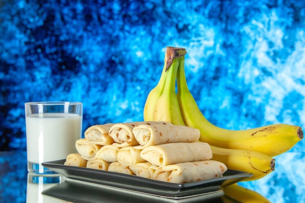 front view yummy rolled pancakes with bananas and milk on a light blue background dessert sugar morning fruit color milk sweet cake