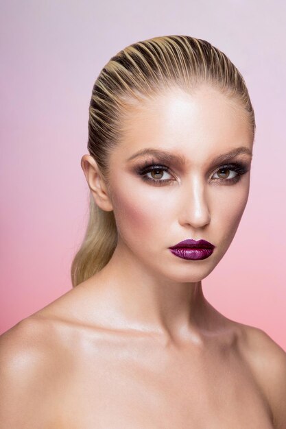 Frontal beauty portrait of a blond woman with makeup isolated pink background