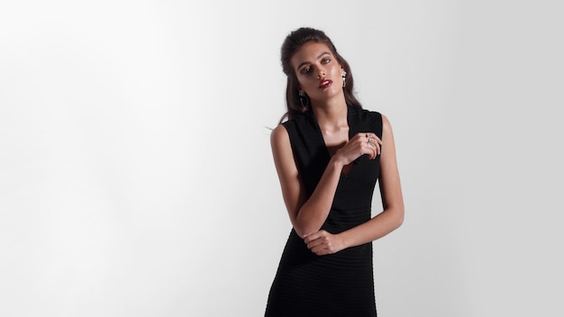 Frontal beauty portrait of a young woman with makeup, red lipstick, dressed in black dress, isolated white background.