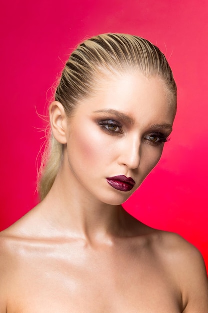 Frontal beauty portrait of young woman with perfect makeup with bare shoulders over red background