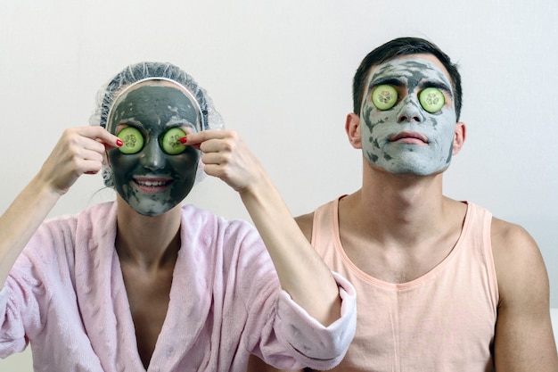 Frontal portrait of a married couple with clay masks on his face and cucumbers in front of him. Spa at home. skin care