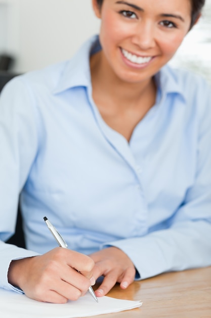 Frontal view of a charming woman writing on a sheet of paper while sitting